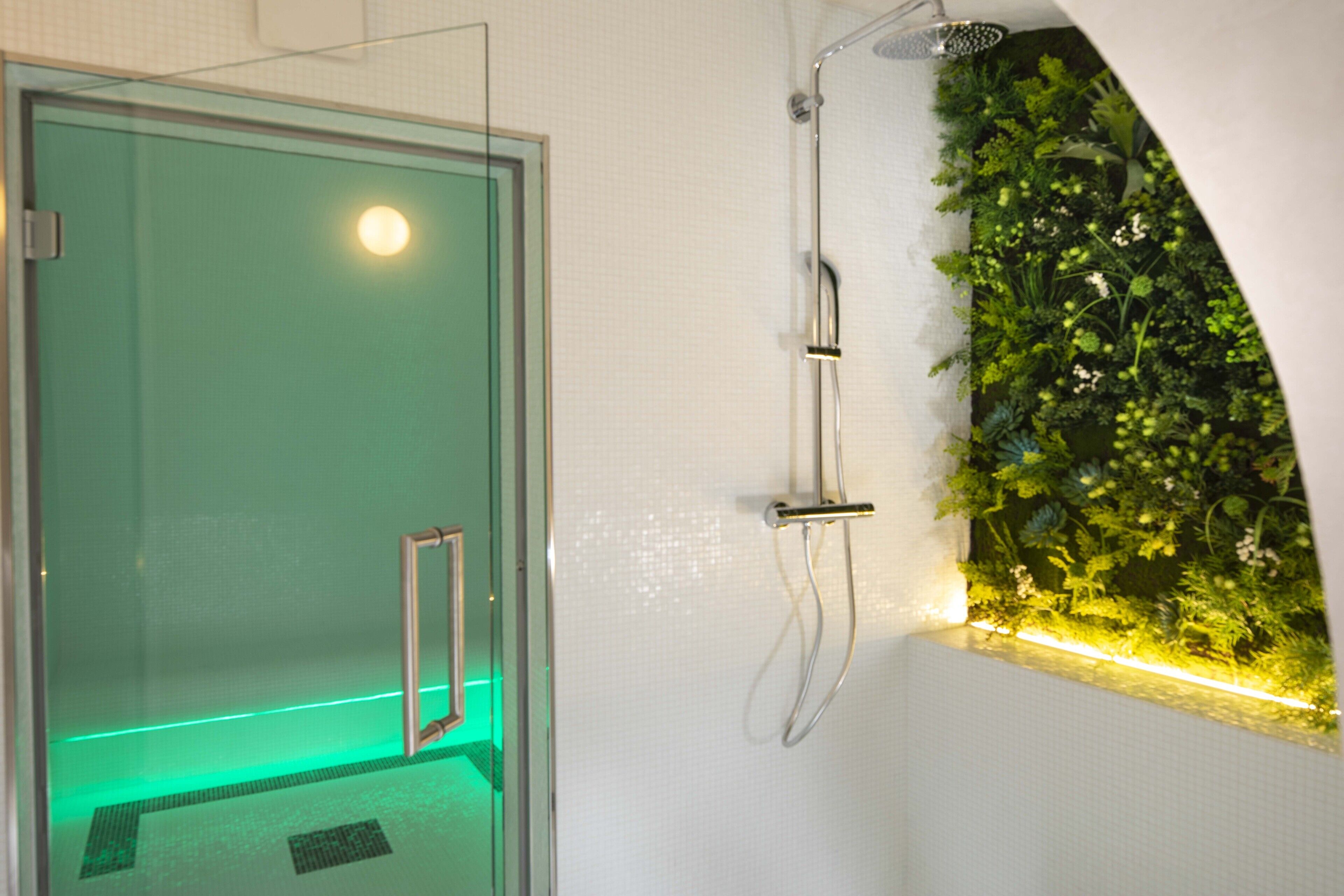 A modern bathroom with a glass-enclosed shower, a wall-mounted rain showerhead, and a green vertical garden.