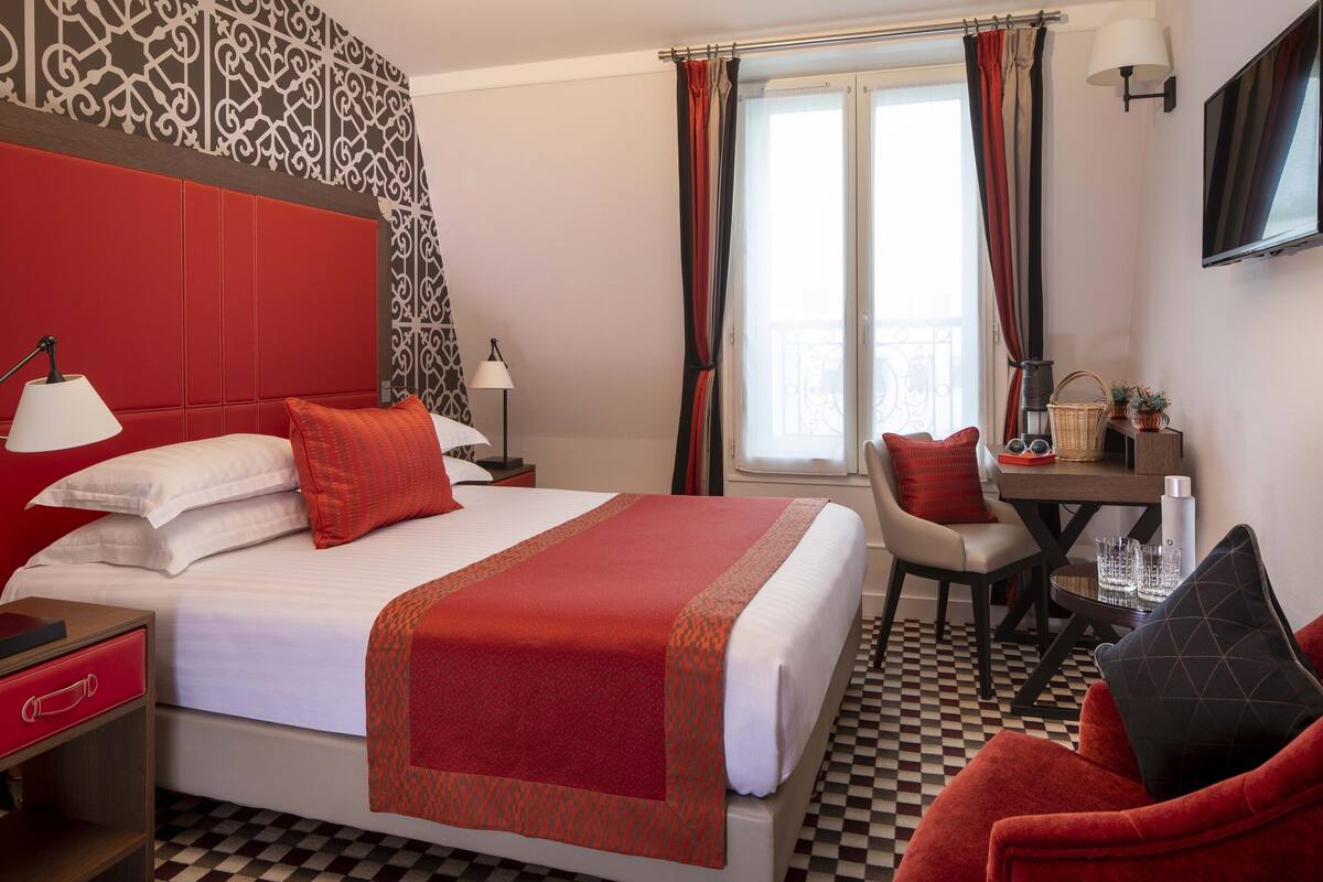 A hotel room with a large bed, a desk, a chair, and a TV.