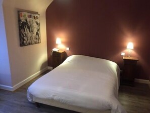 Un dormitorio con una cama, dos mesitas de noche, una lámpara de pared y un cuadro enmarcado.