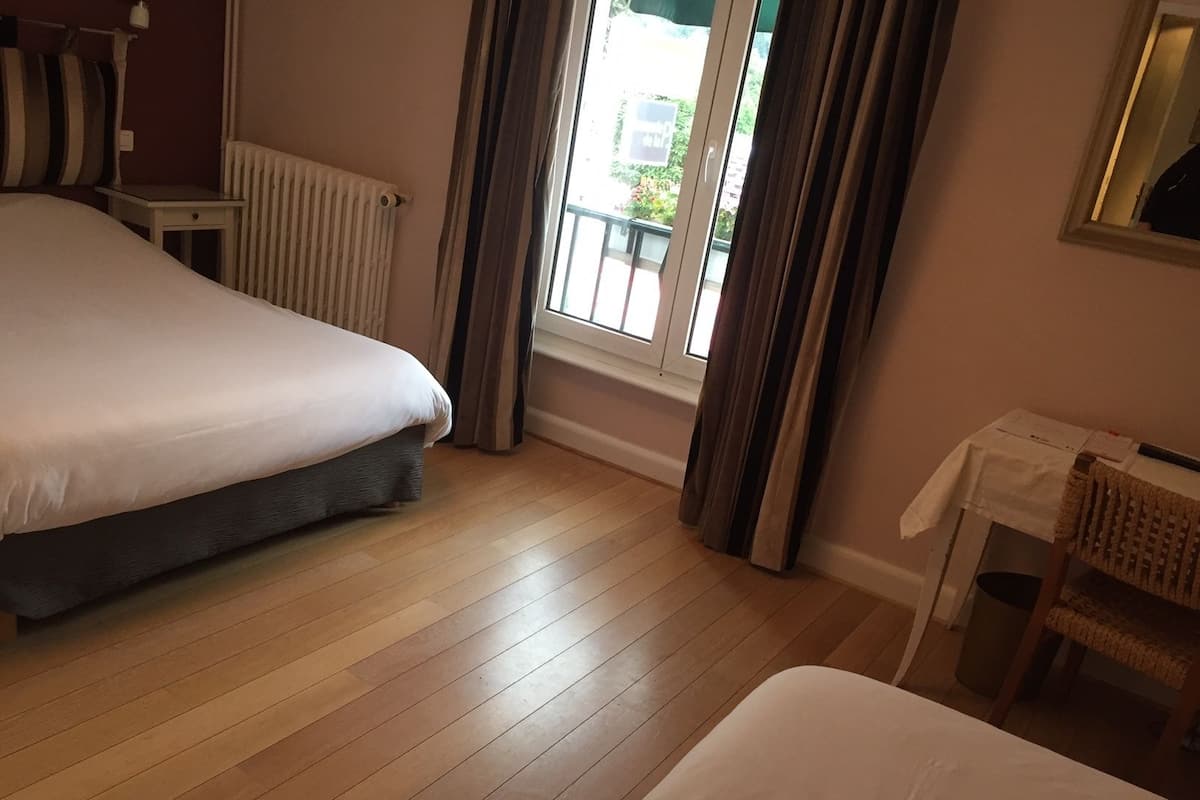 Ett hotellrum med två sängar, ett element, ett fönster med gardiner, ett litet bord med en stol och en spegel på väggen.