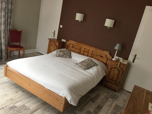 Un dormitorio con una cama de madera, dos mesitas de noche, una silla roja y una puerta.