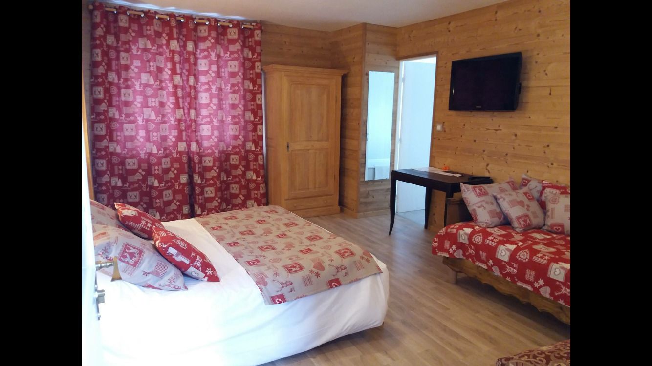 A room with a bed, a sofa, a television, and a wooden wardrobe.