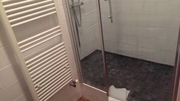 A shower with a glass door, a white towel hanging on the door, and a tiled floor.