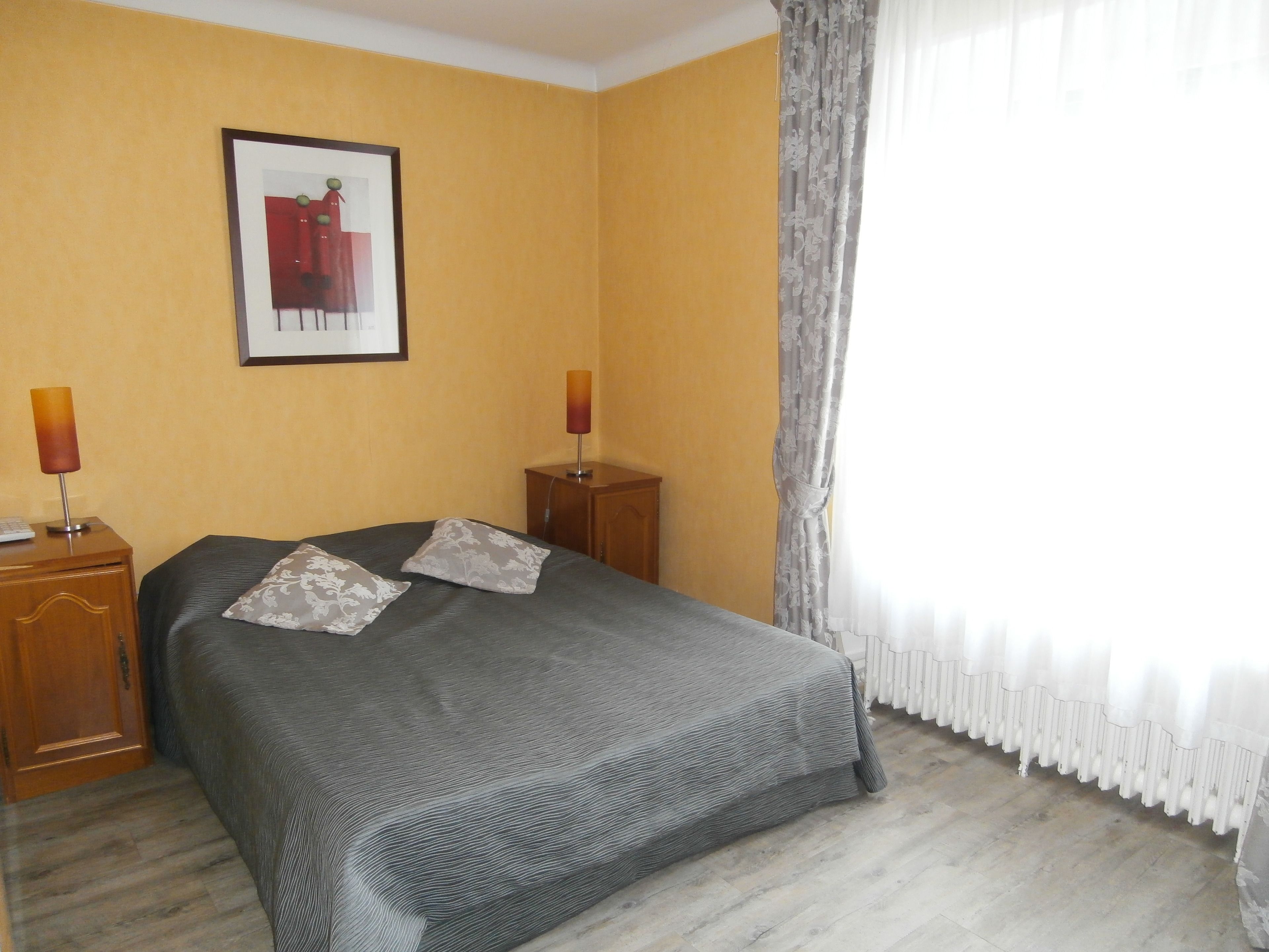 Una habitación de hotel con una cama, dos mesitas de noche, una lámpara, un cuadro en la pared y una ventana con cortinas.
