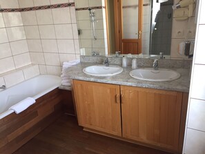 Un baño con dos lavamanos, una bañera, armarios de madera y un espejo.