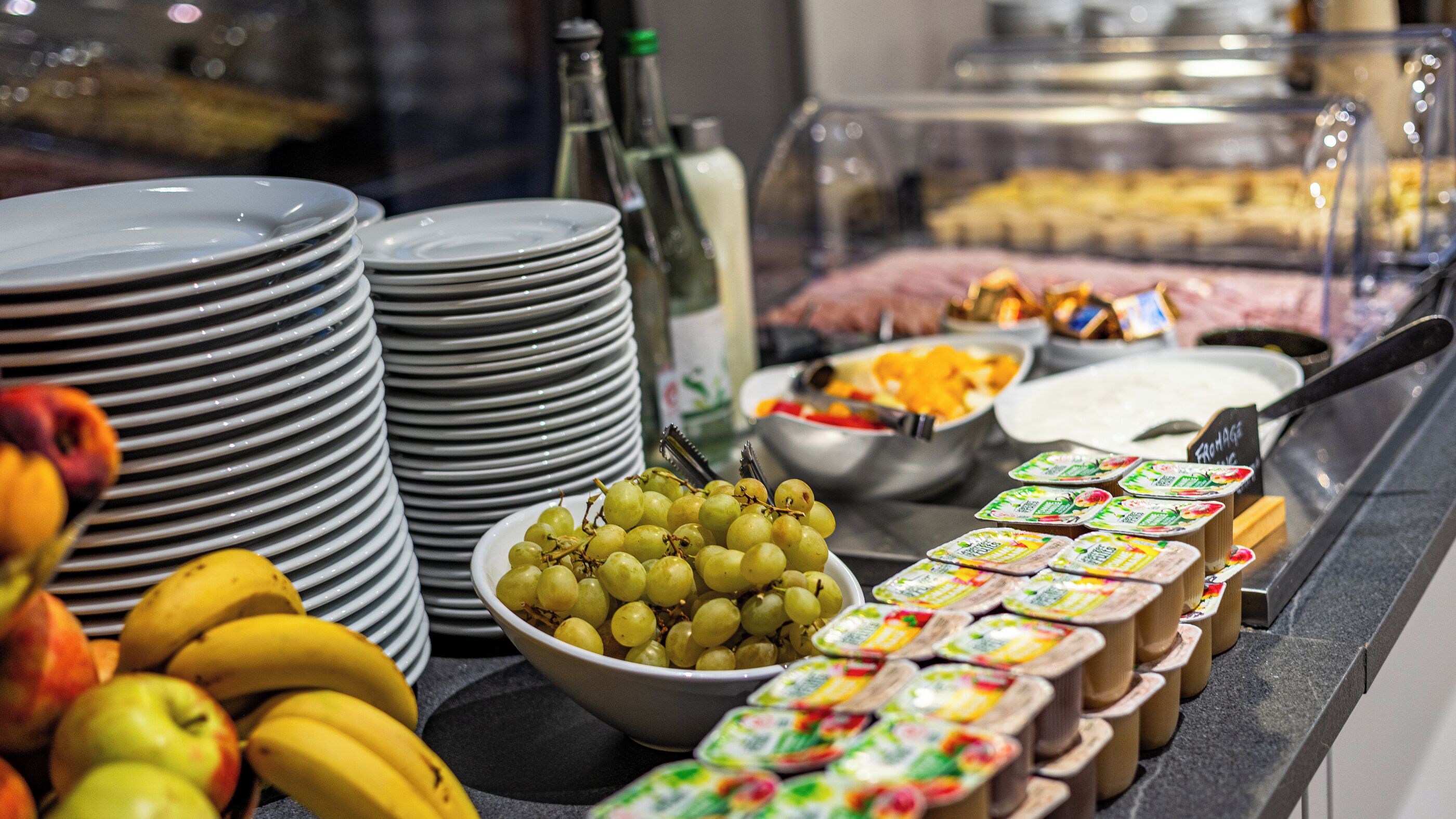 A buffet with plates, bowls of fruit, and various food items.