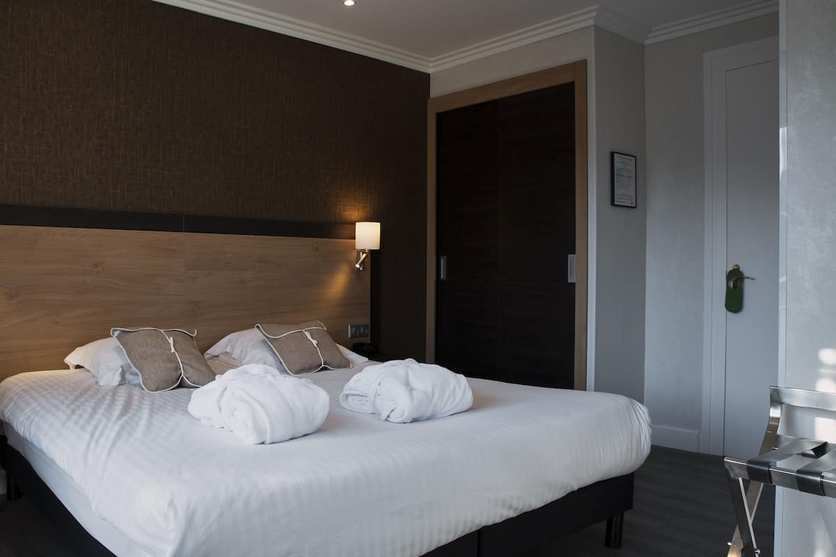 A hotel room with a large bed, two bedside lamps, a wooden headboard, and a door with a green handle.