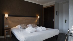 A hotel room with a large bed, two bedside lamps, a wooden headboard, and a door with a green handle.