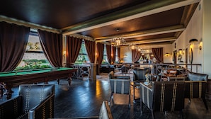 A billiards room with a pool table, leather chairs, and a bar area with a view of the outdoors. - Hôtel Beau Rivage (Gerardmer)