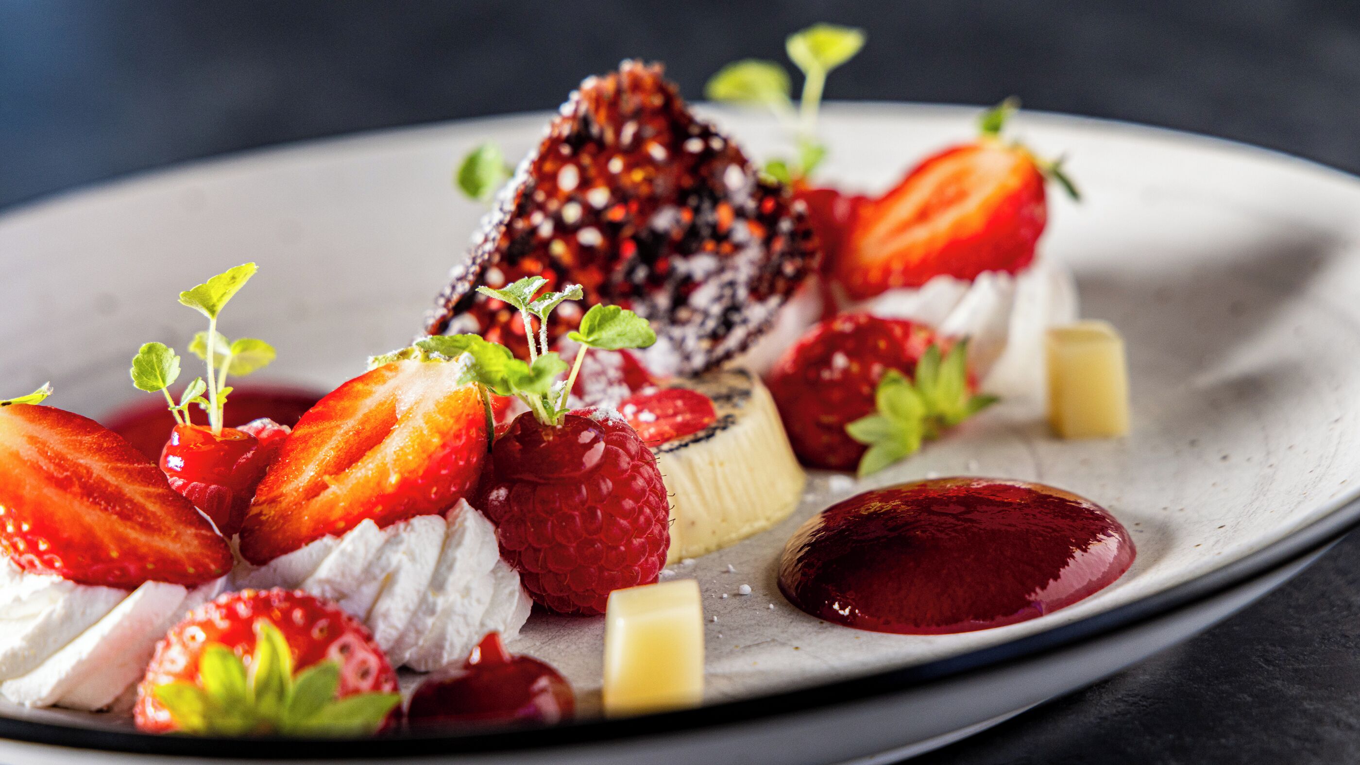 Une assiette de dessert garnie de fraises, de framboises, de crème fouettée et d’un dessert enrobé de chocolat.