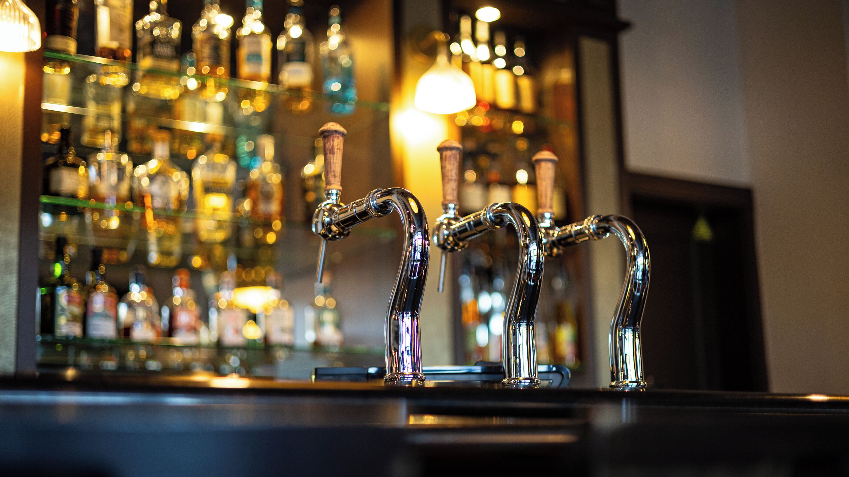 A bar with multiple taps and a variety of bottles in the background.