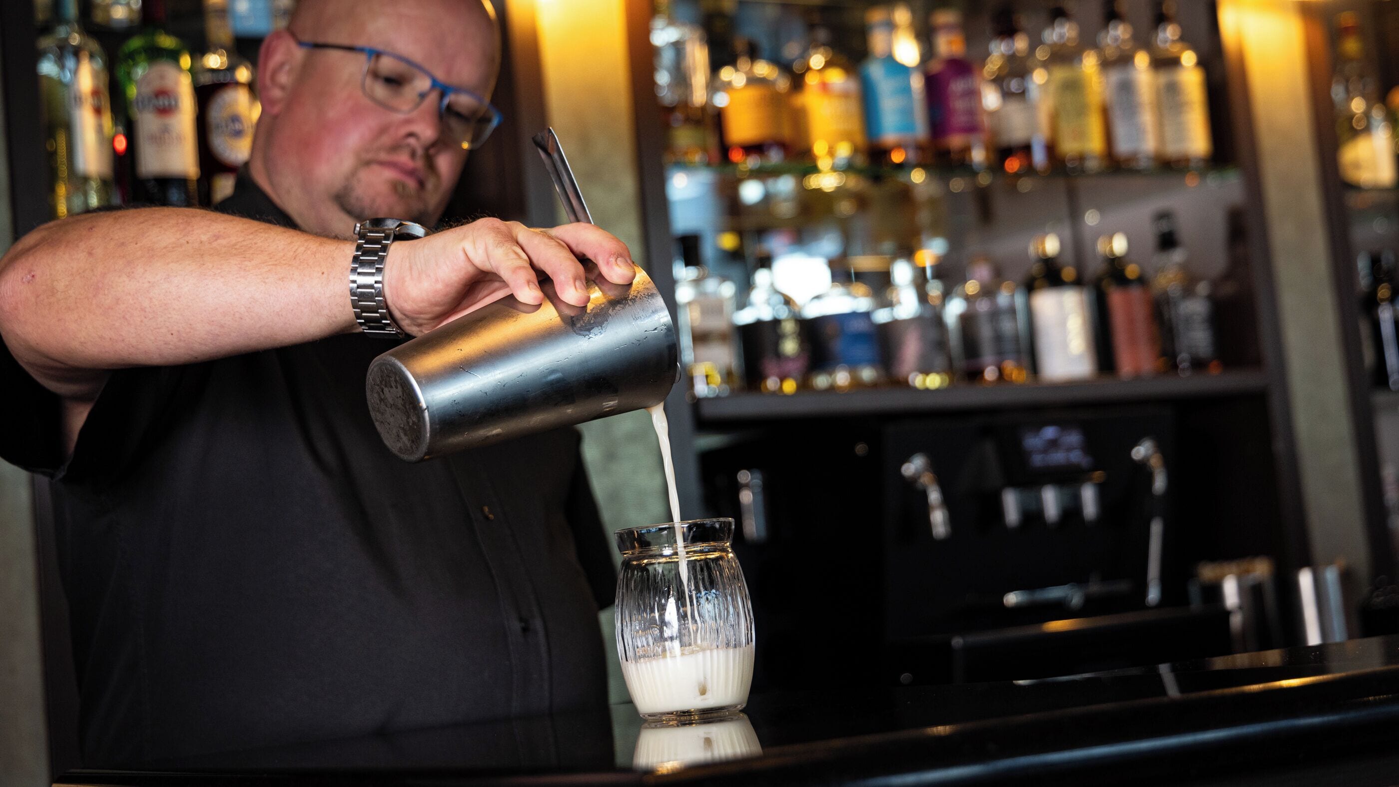 A bartender pouring a drink into a glass.