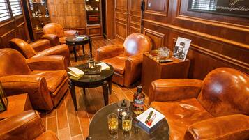 A room with leather armchairs, a round table, and a bar area with a framed photo and a menu.