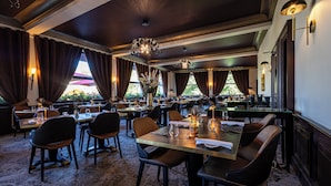 A restaurant with multiple tables and chairs, large windows with curtains, and a chandelier. - Hôtel Beau Rivage (Gerardmer)