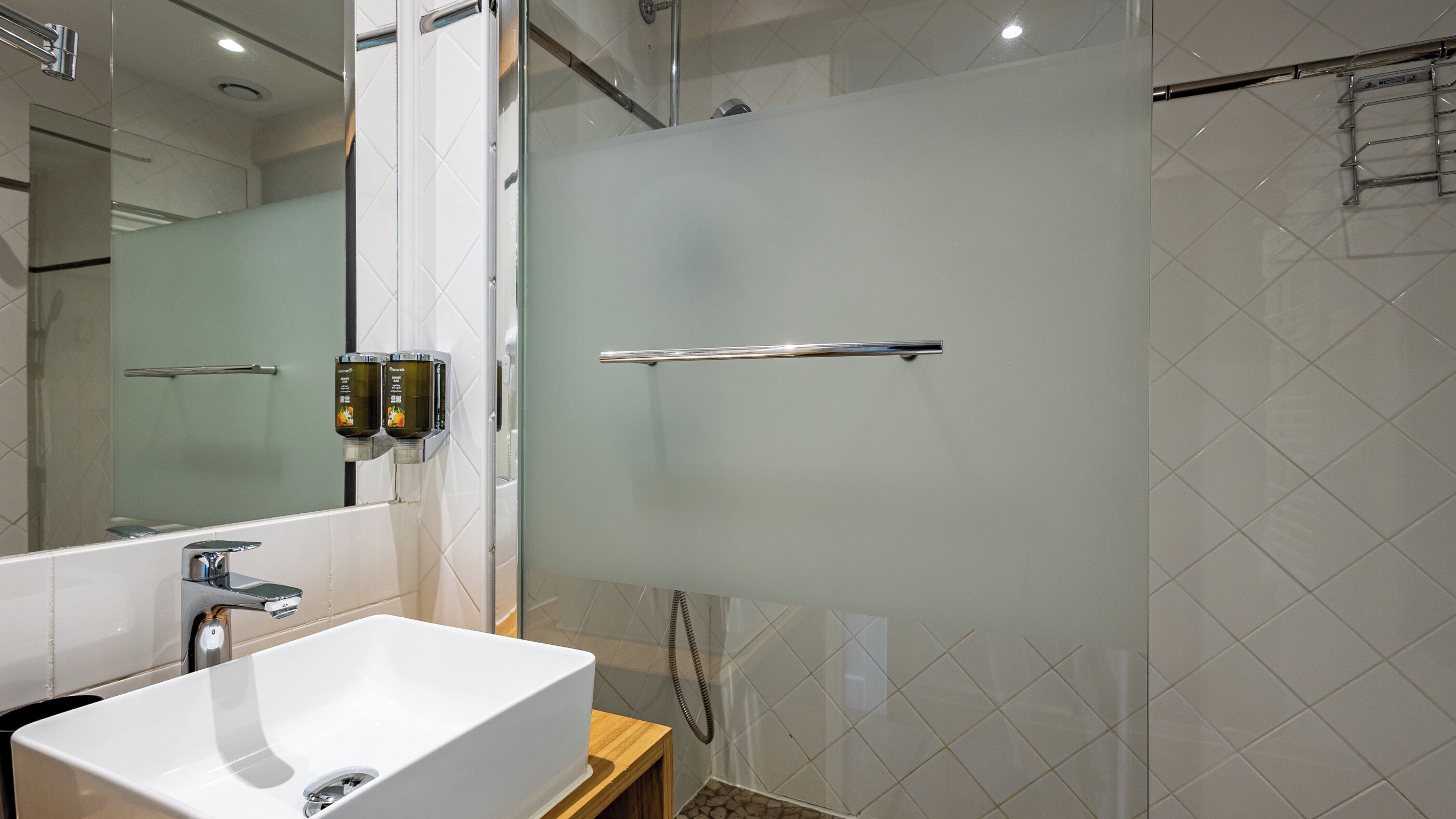 A modern bathroom with a white sink, a glass shower enclosure, and a hand dryer mounted on the wall.