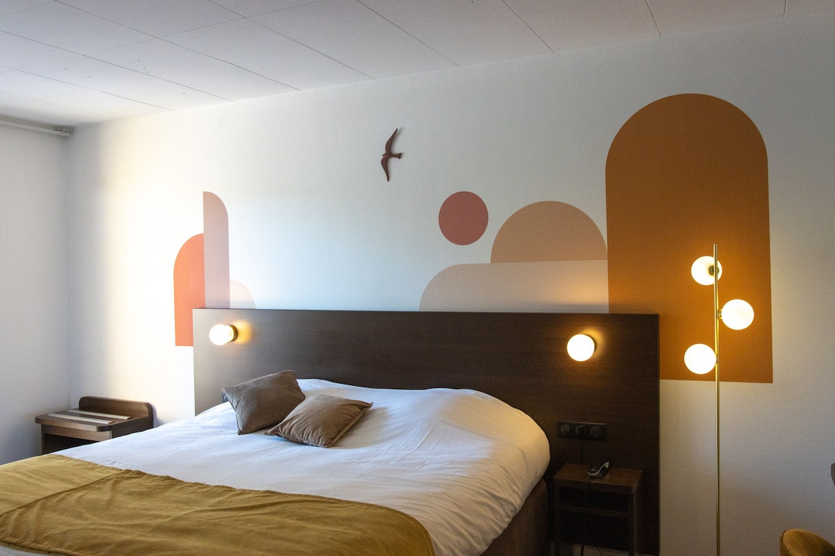 A modern hotel room with a large bed, a nightstand, and a wall-mounted light fixture.