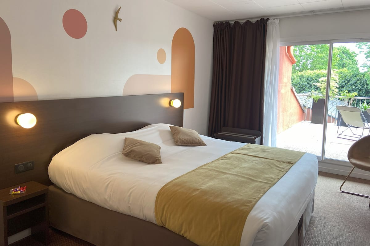 A hotel room with a bed, bedside tables, a window with curtains, and a view of the outdoors.
