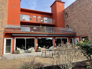 A two-story building with a red exterior, a covered patio area with outdoor seating, and a brick wall adjacent to it. - Le Relais De Montigny - Logis (Montigny)