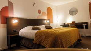 A hotel room with a bed, bedside tables, a desk, a chair, a mirror, and a wall with abstract art. - Le Relais De Montigny - Logis (Montigny)