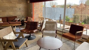 A modern living room with a large window, leather sofas, and a variety of chairs. - Le Relais De Montigny - Logis (Montigny)