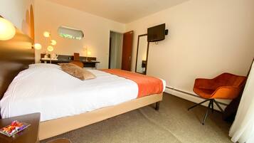 Habitación de hotel con cama, escritorio con lámpara, silla, televisión y espejo.