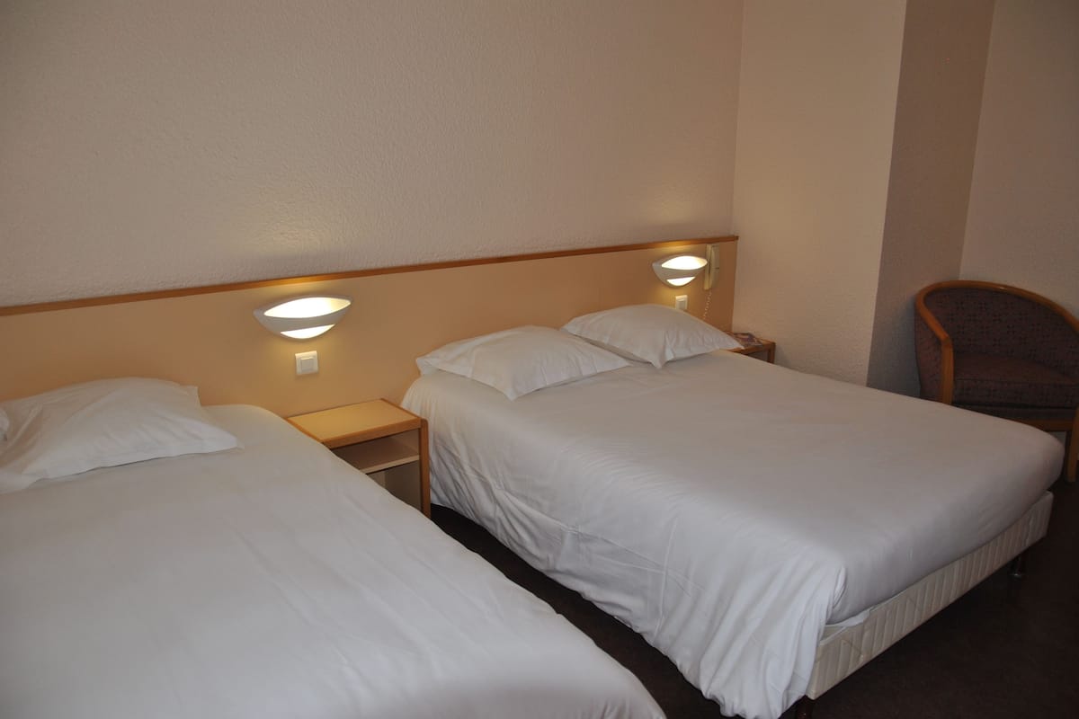 A hotel room with two single beds, each with a nightstand and a wall-mounted lamp.