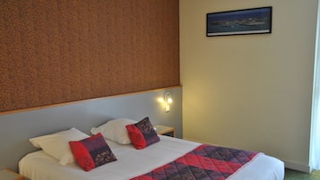 Una camera d'albergo con un letto, due cuscini, un comodino, una lampada a parete e un quadro appeso al muro.