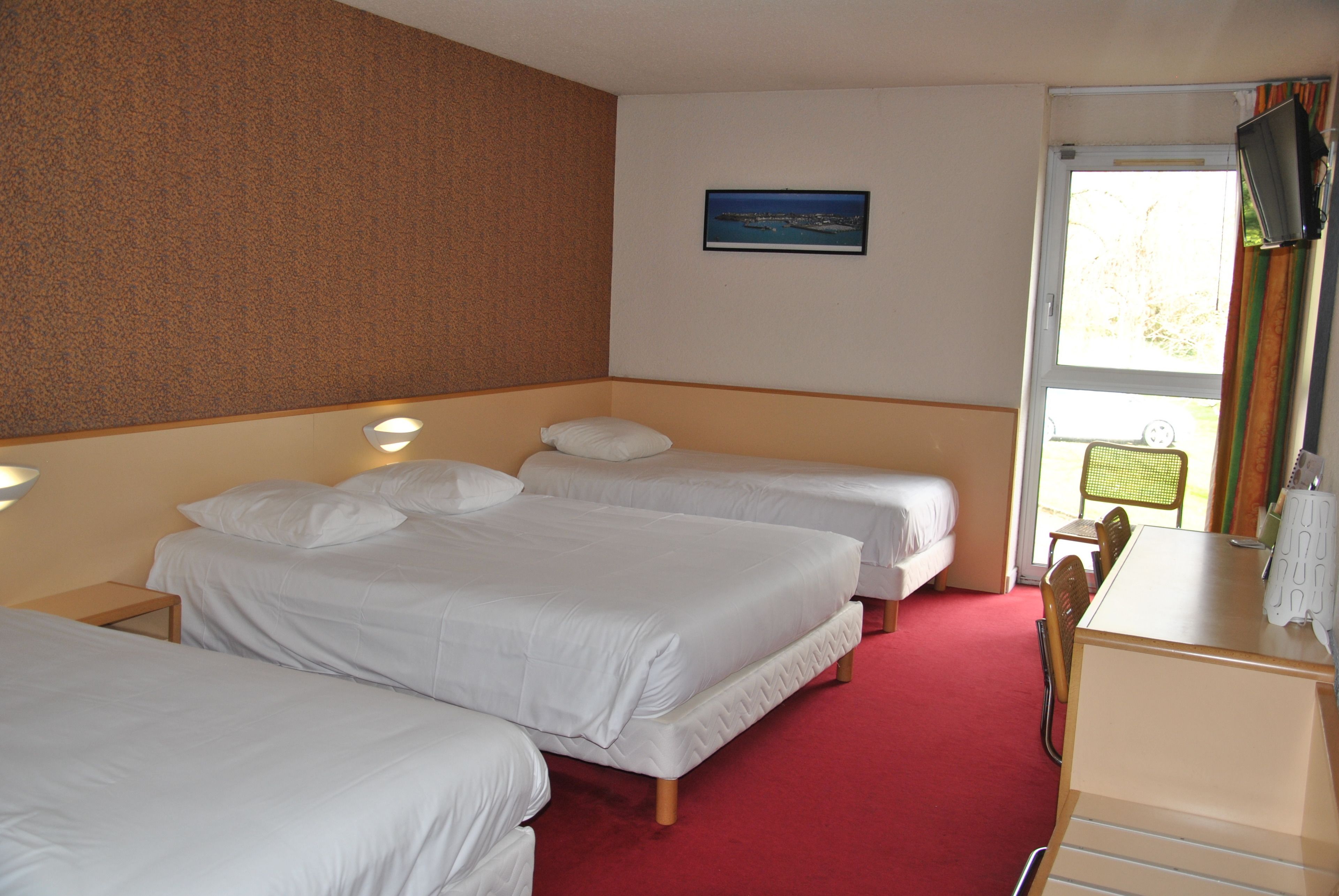 A hotel room with three single beds, a desk, and a chair.