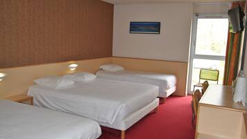 A hotel room with three single beds, a desk, and a chair.