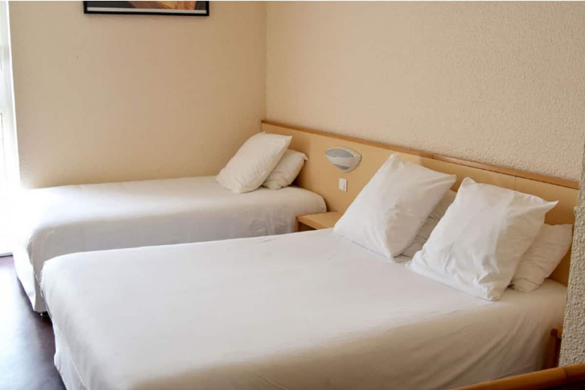 A hotel room with two single beds, each with white bedding and pillows.