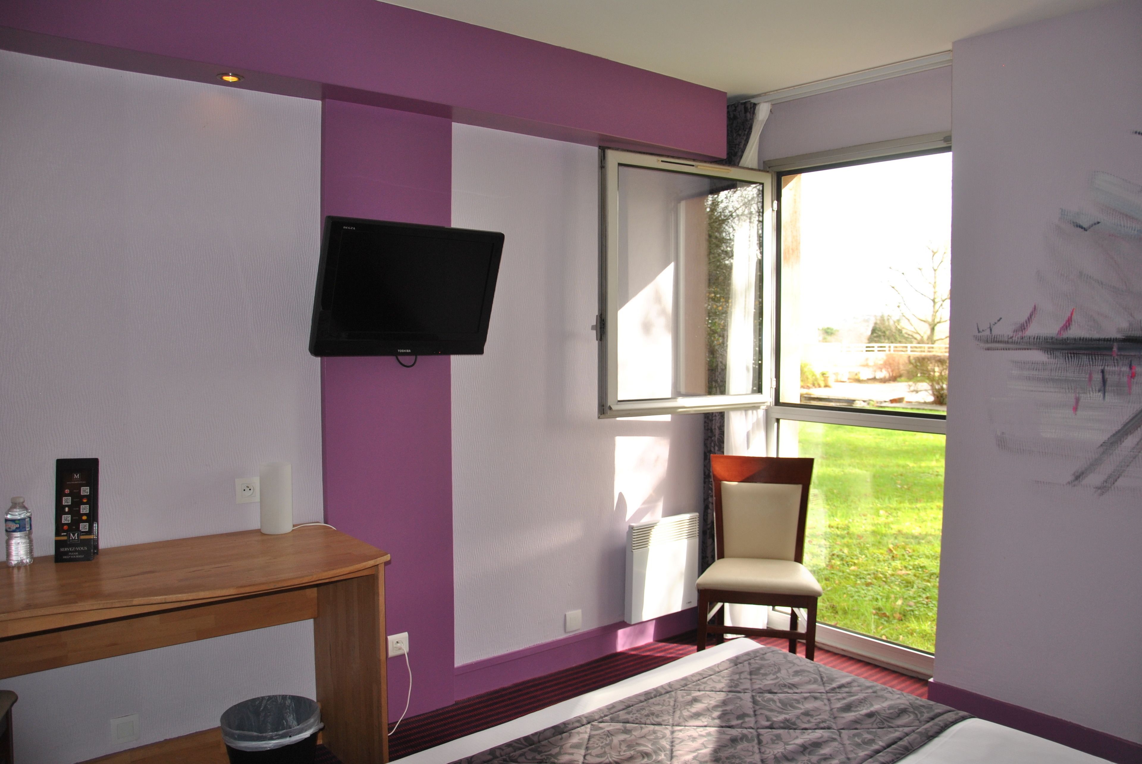 A room with a bed, a television mounted on the wall, a chair, and a window with a view of the outdoors.