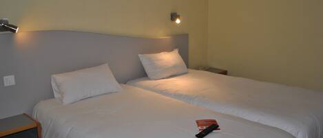 A double bed with white bedding, a bedside table, a nightstand, and a wall-mounted light fixture.