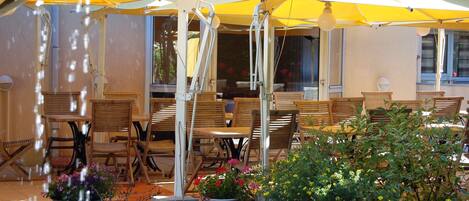 An outdoor seating area with wooden tables and chairs, yellow umbrellas, and potted plants.