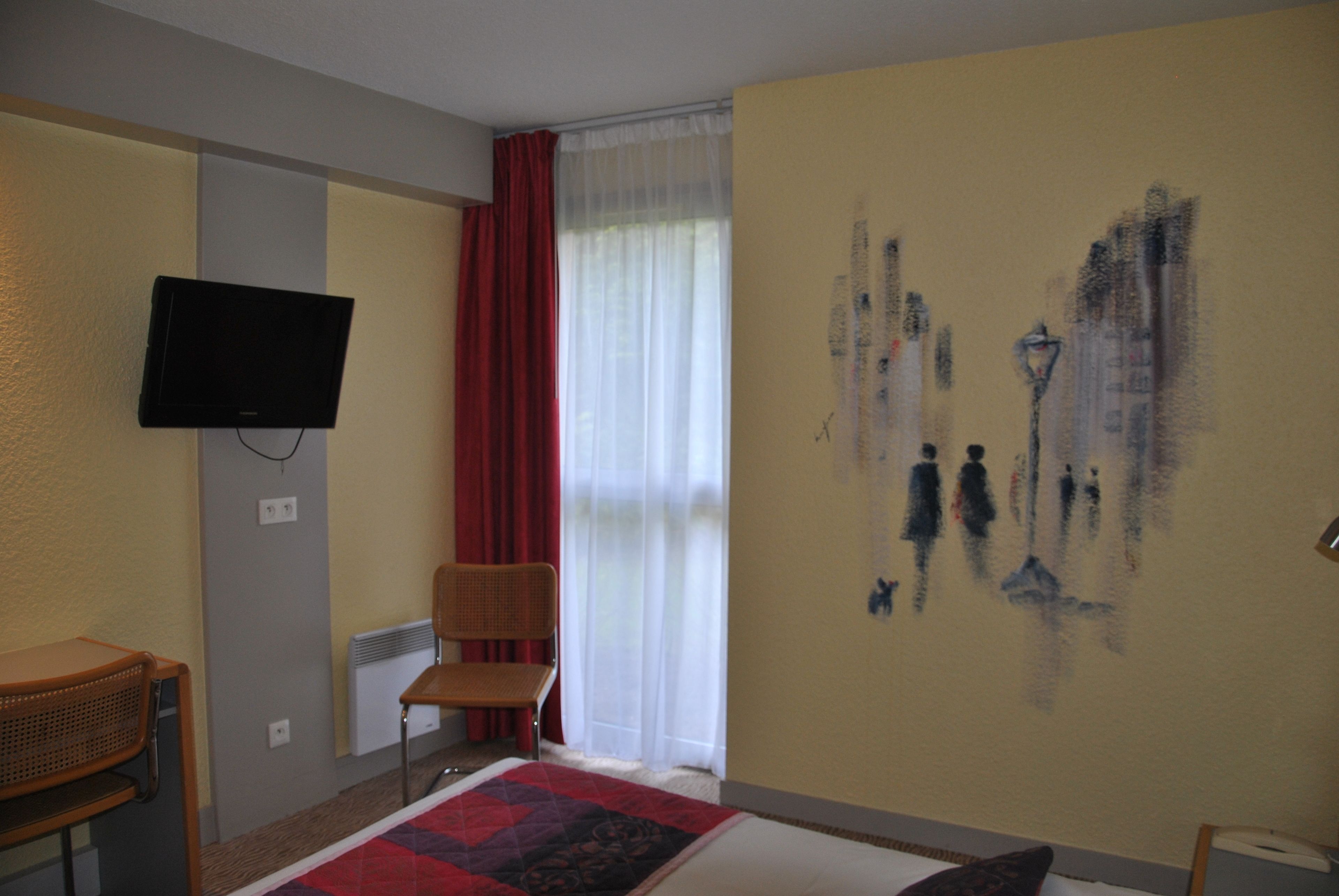 A hotel room with a bed, a chair, a television, a window with curtains, and a wall with a painting.