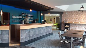 A modern bar area with a counter, shelves of bottles, and a seating area with tables and chairs. - Hôtel Cositel Coutances (Coutances)