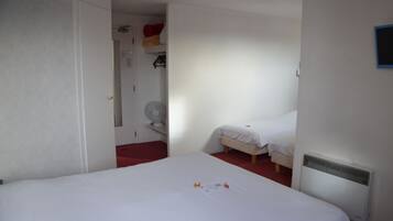 Una habitación con una cama grande, una cama más pequeña, un calentador y una puerta que da a otra habitación.