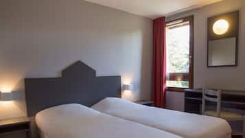 Une chambre d’hôtel avec un lit double, des lampes de chevet, un bureau avec une chaise, une fenêtre avec des rideaux et un luminaire fixé au mur.