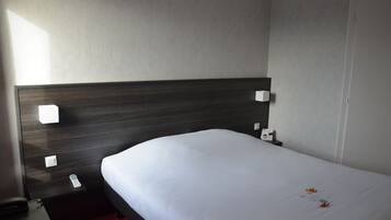 Habitación de hotel con tablero de cama de madera oscura, colcha blanca y control remoto sobre la mesita de noche.