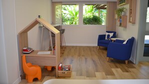 A room with a play area, a desk, a blue sofa, and a window with a view of greenery.
