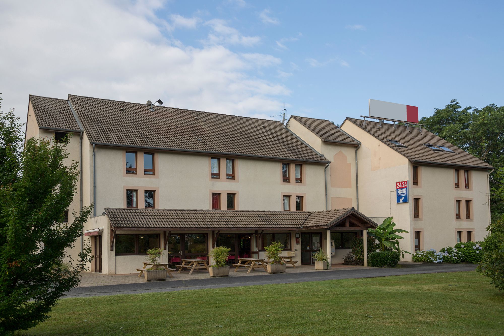A two-story building with a tiled roof, multiple windows, and a covered outdoor seating area with tables and chairs.