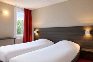 Ein Hotelzimmer mit zwei Betten, einem Fenster mit roten Vorhängen und Wandleuchten.