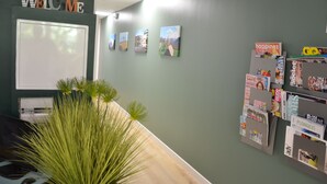 A reception area with a 'WELCOME' sign, a whiteboard, a plant, and a bulletin board with magazines and a 'happiness' sign.