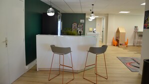 A modern office space with a reception desk, two bar stools, a green accent wall, and a wooden floor.