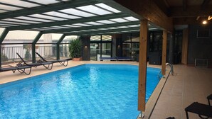 An indoor swimming pool with clear blue water, surrounded by lounge chairs and a glass ceiling. - Logis Hotel la Résidence (Le Val-d'Ajol)