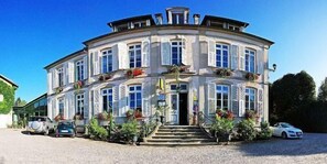 A multi-story building with a curved facade, a central entrance with steps, and a driveway with parked cars. - Logis Hotel la Résidence (Le Val-d'Ajol)