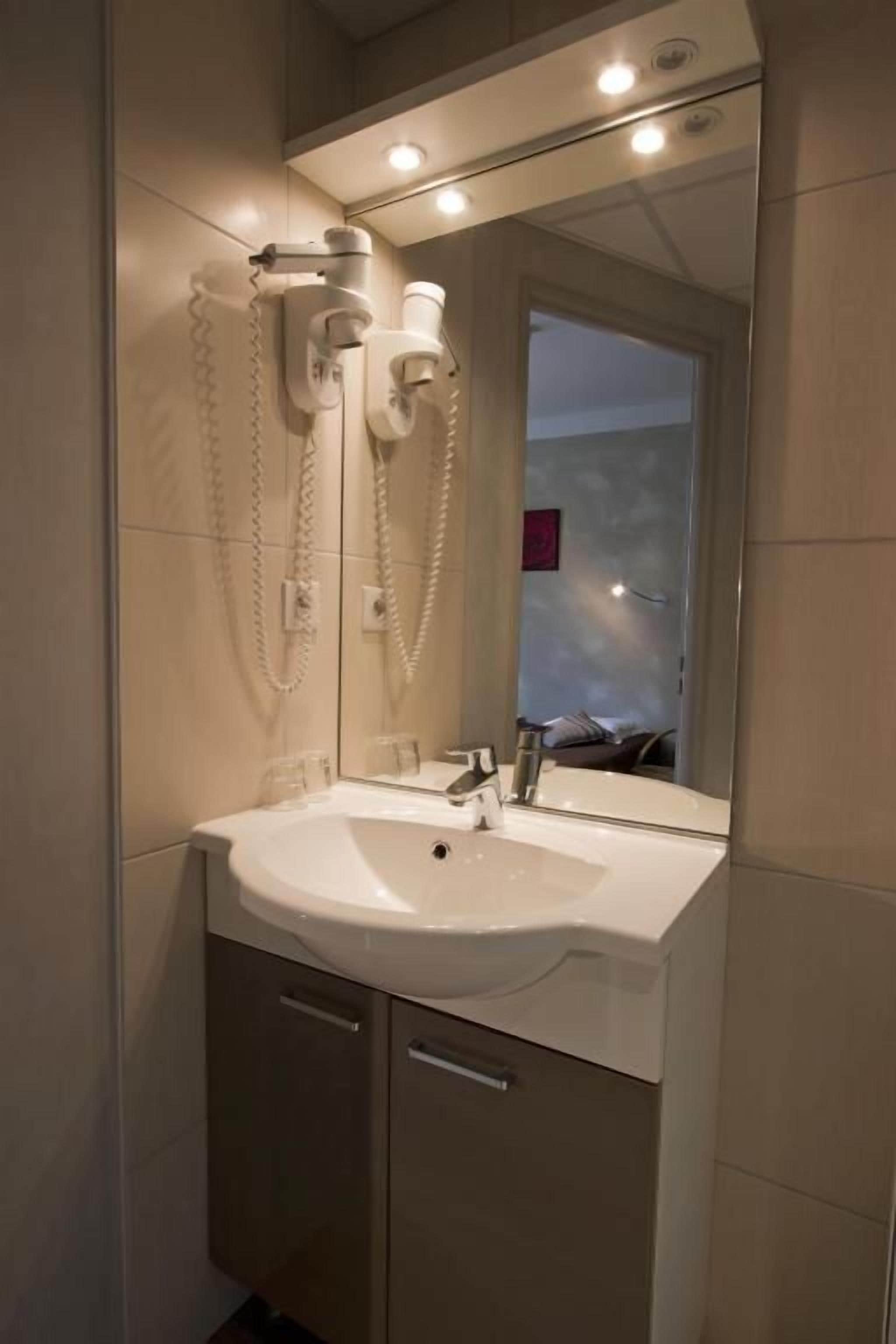 Un bagno con un lavandino bianco, uno specchio e un asciugacapelli montato a parete.