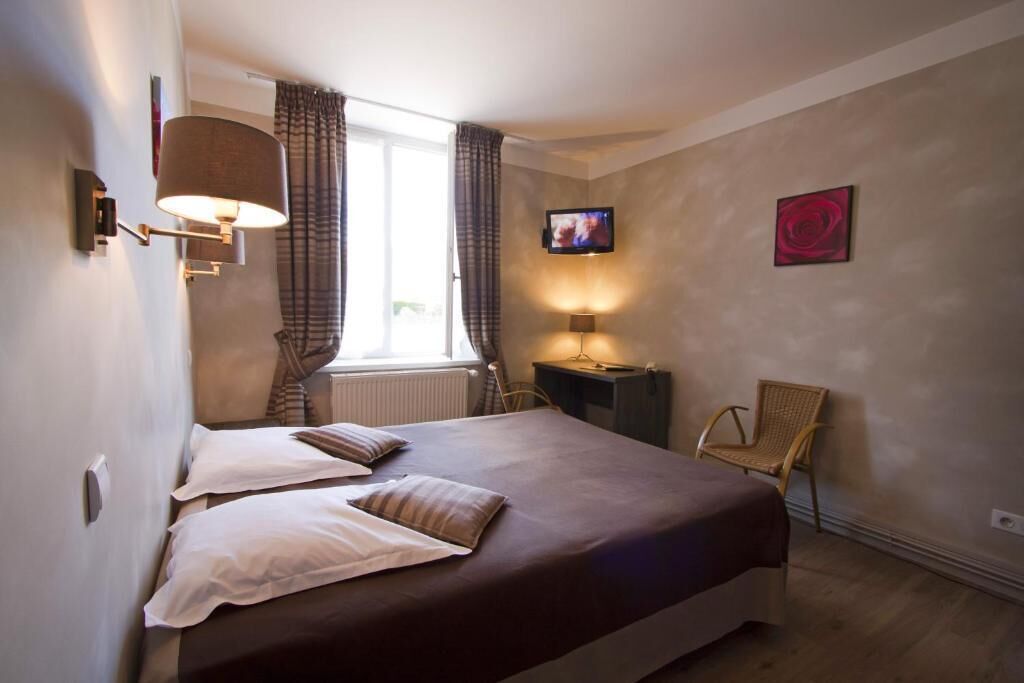 A bedroom with a bed, two bedside lamps, a TV, a chair, and a window with curtains.