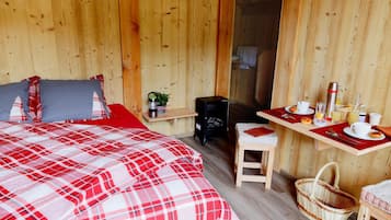 Una habitación de madera con una cama, una mesita con alimentos para el desayuno, una silla y una cesta.