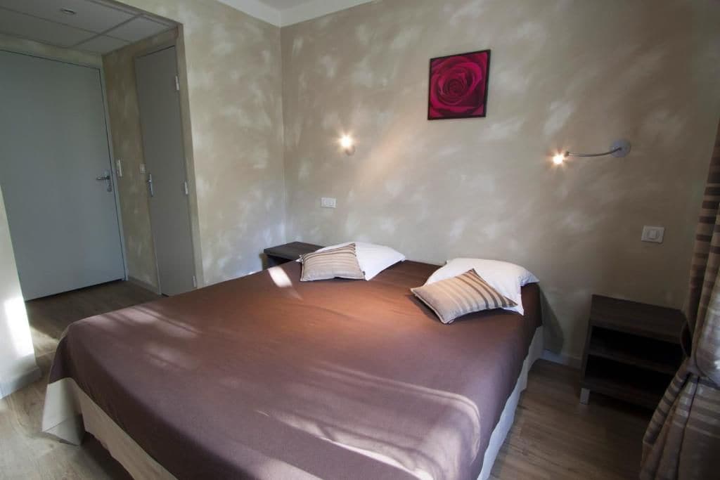A bedroom with a large bed, bedside tables, a wall-mounted light, and a door.
