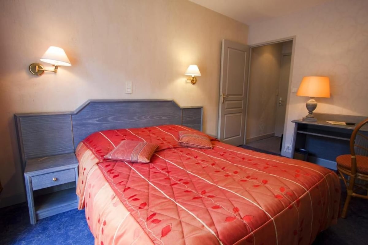 Un dormitorio con cama, mesitas de noche, escritorio, silla y dos lámparas de pared.